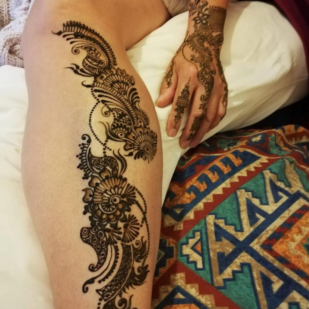 Henna design on a person's leg and hand with a colorful patterned rug in the background