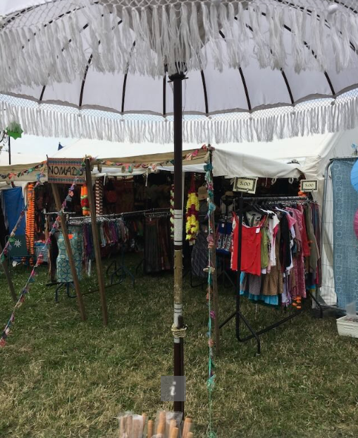 Outdoor market stall with clothing and accessories under a large white umbrella.