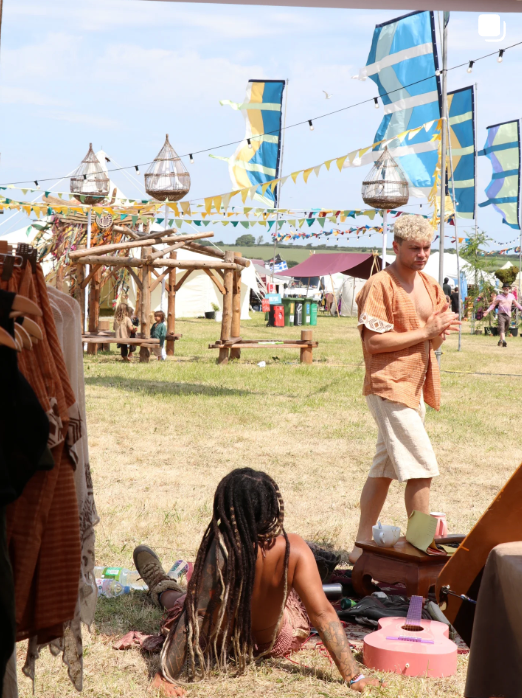Two people at a festival with wooden stalls and colorful flags in the background.